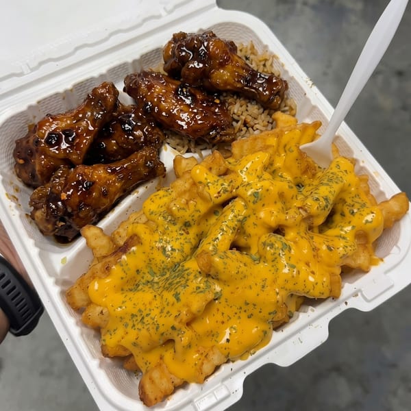Takeout container with glazed chicken wings over rice and waffle fries smothered in cheese sauce.